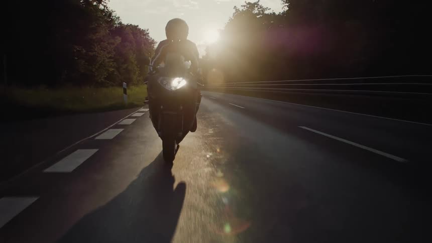 A person is riding a motorcycle down a road at sunset