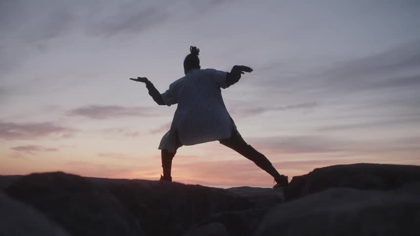 Person moves through pose standing on boulders under a red sky