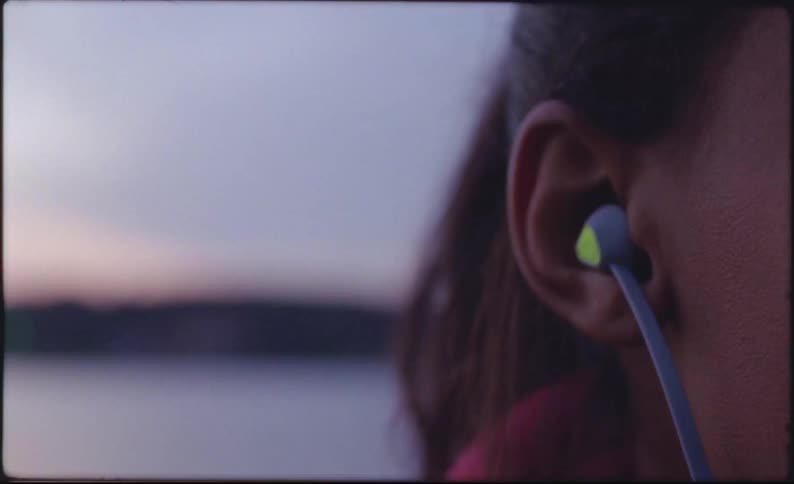 A woman puts a wired earbud in her ear while standing outside in the snow