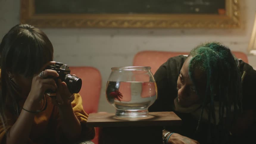 Woman watches fish in fish bowl and talks to woman taking picture of fish