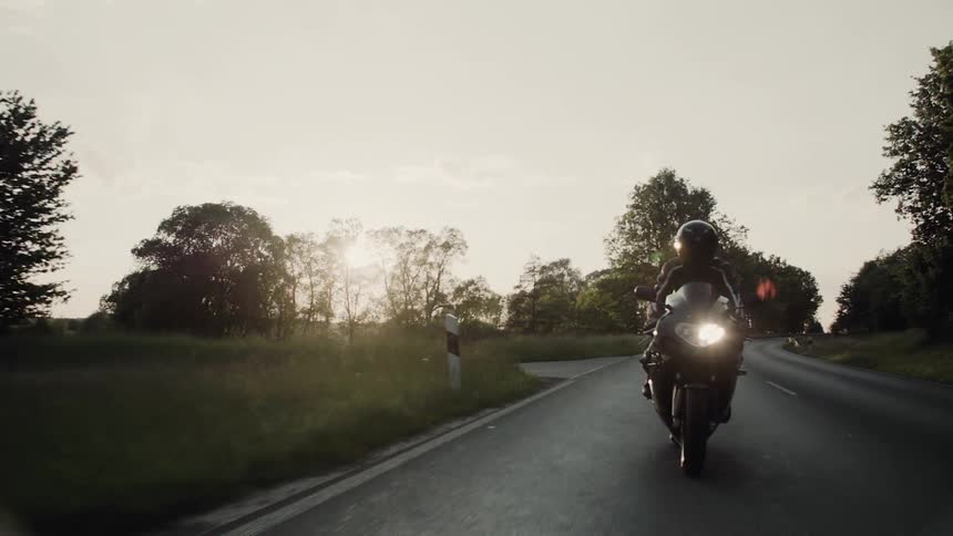 A motorcycle is riding down a road at sunset