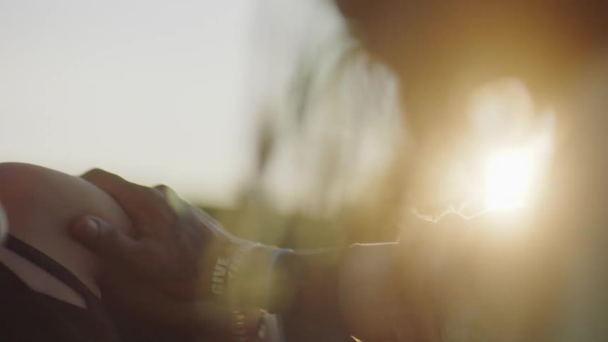 A man touches his girlfriends arm as they lie on their sides in a field