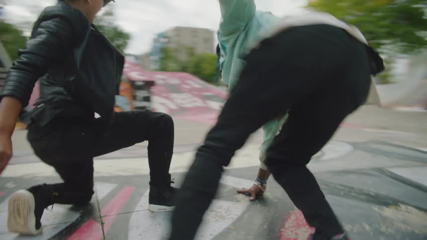 A teenage boy and girl dance on painted pavement in a park