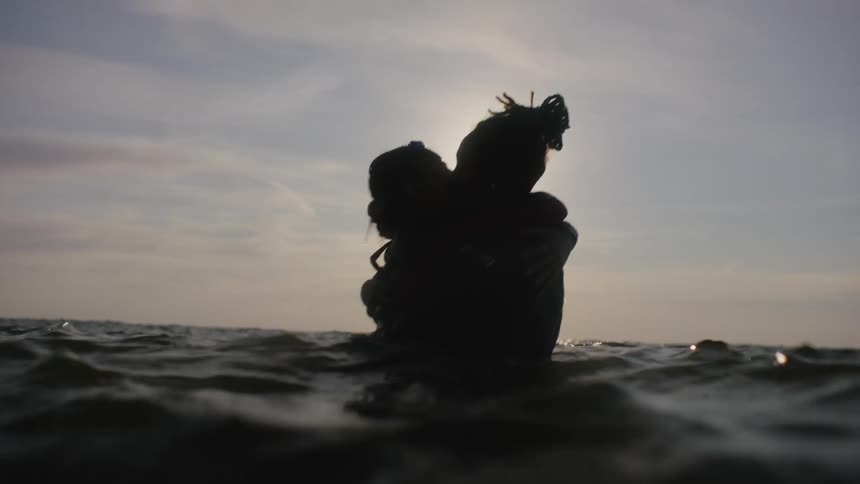 Silhouette of a young couple hugging and kissing while standing in the ocean at sunset
