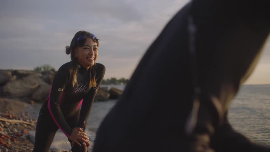 Woman wearing wet suitstretches on ocean shore then cartwheels backward while playing with another person
