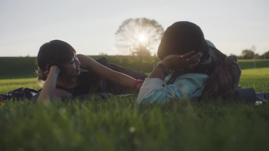 A woman touches her boyfriends hand as they lie in the grass