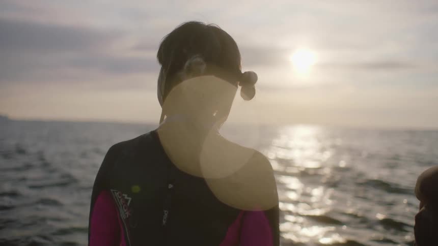 People stand in water wearing wet suit and looking out to horizon