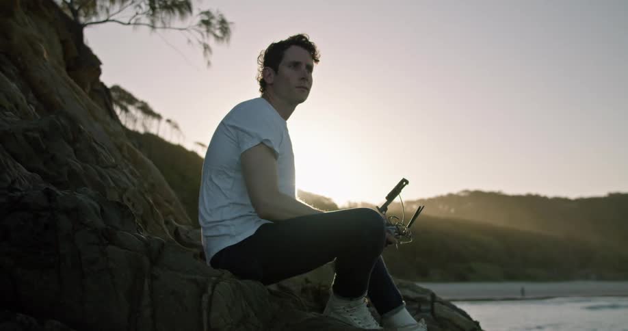 Man sitting on slope on shore gestures while holding controller