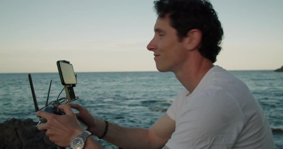 Man with white t shirt flies drone using drone remote controller on the coast