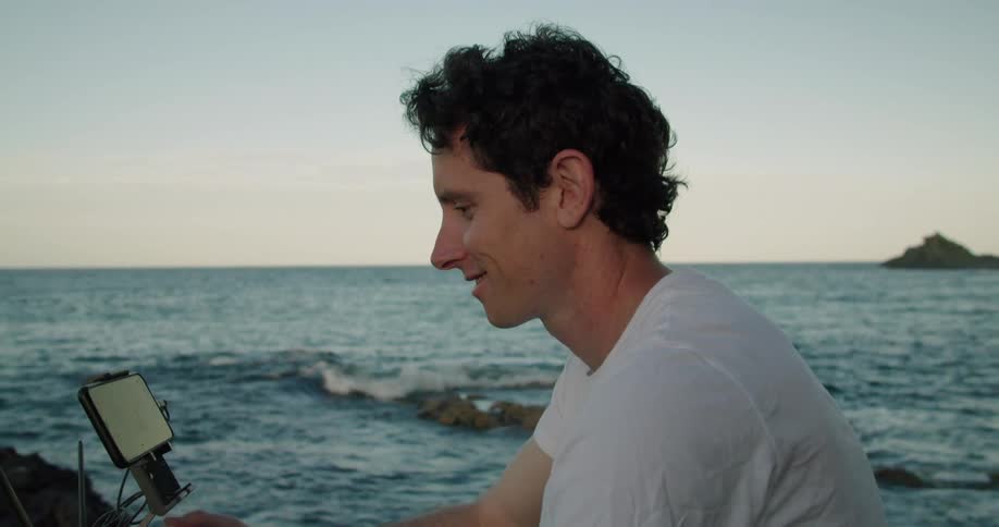 A man sits on the shore and uses a drone