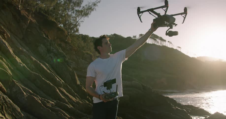 A man standing on the coast uses a radio controller to pilot a drone close enough for him to grab it and carry it away