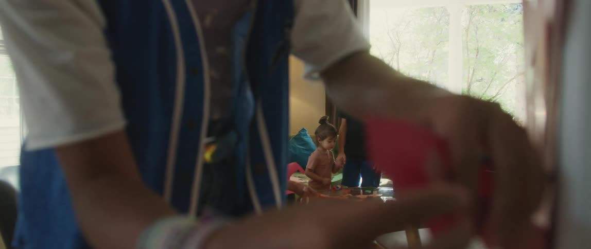 A family is in their home making decorations from colored construction paper as someone tapes one of them on a wall