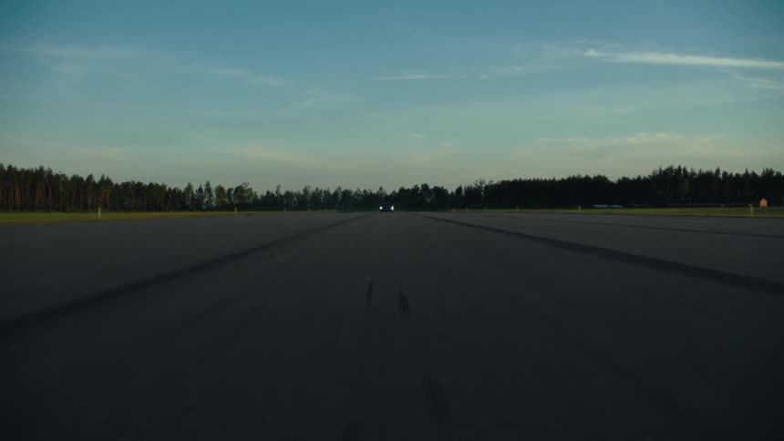 A car travels forward on an empty track with headlights on