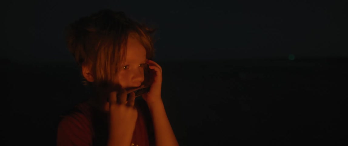 A boy plays a harmonica outdoors at night