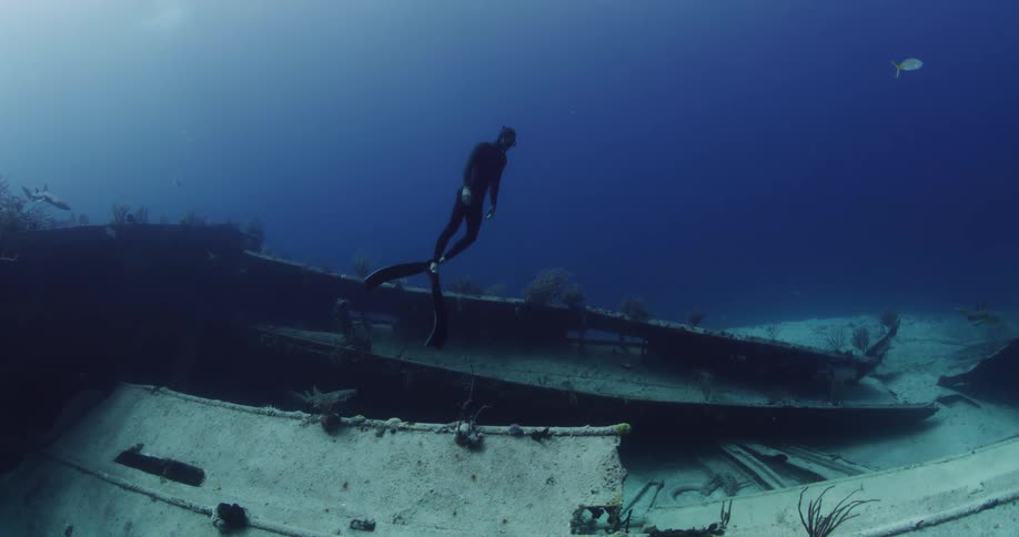 A scuba diver is swimming underwater near sunken ship wreckage