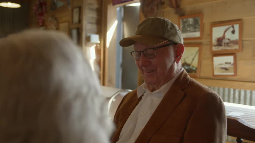 An elderly man sits in a restaurant and talks with a woman