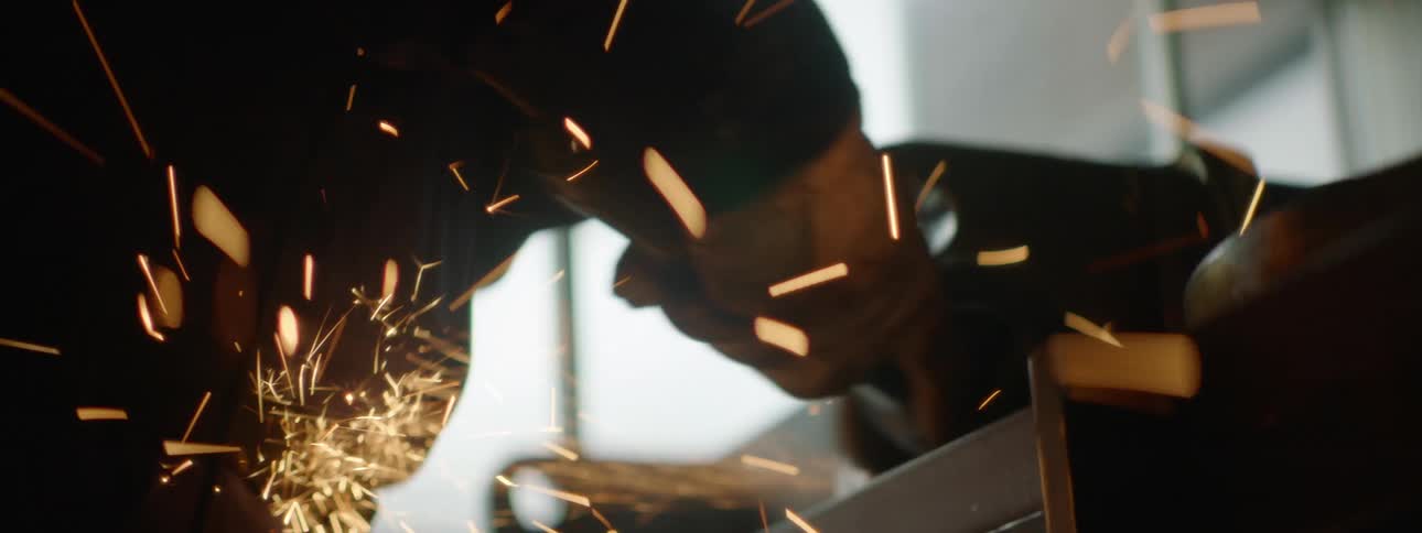 Sparks fly while a construction worker uses a hand held power tool on metal