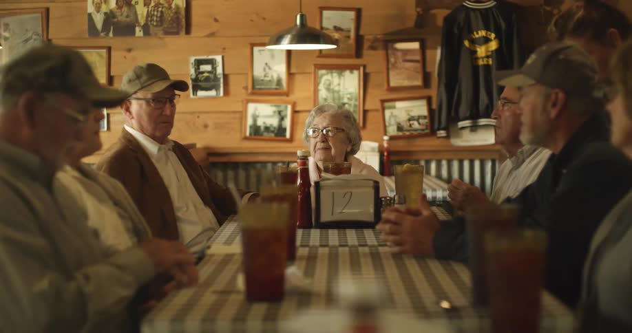 An elderly man speaks to a group of elderly people sitting with him at a table in a restaurant