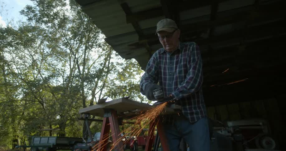 Sparks fly as an elderly man uses a tool outside his workshop