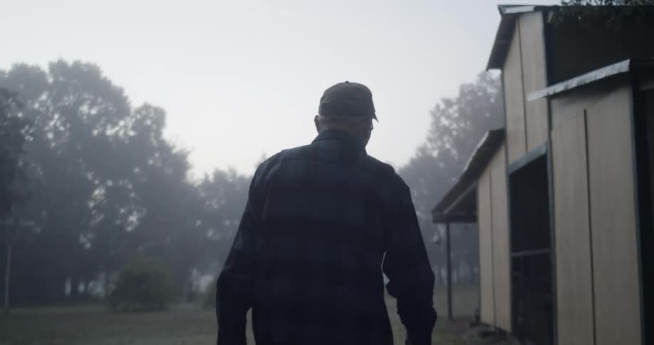 An elderly man is walking toward a garage on a property surrounded by trees on a foggy day