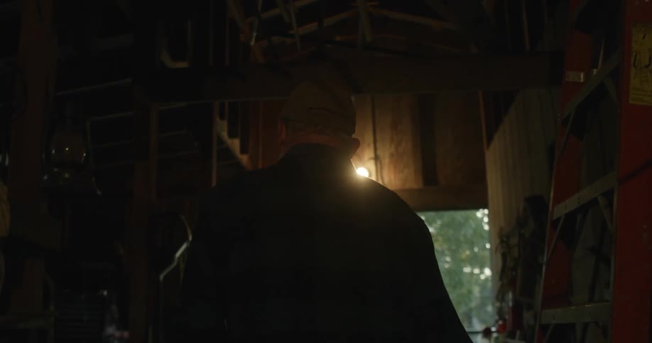 Elderly man walking through a dimly lit shed