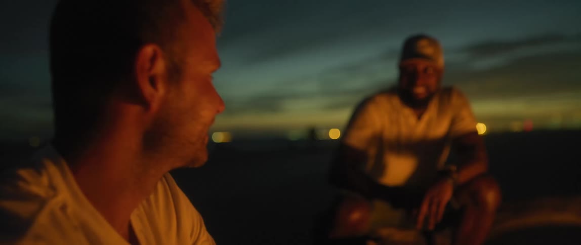 Two men sitting outside next to a fire talking