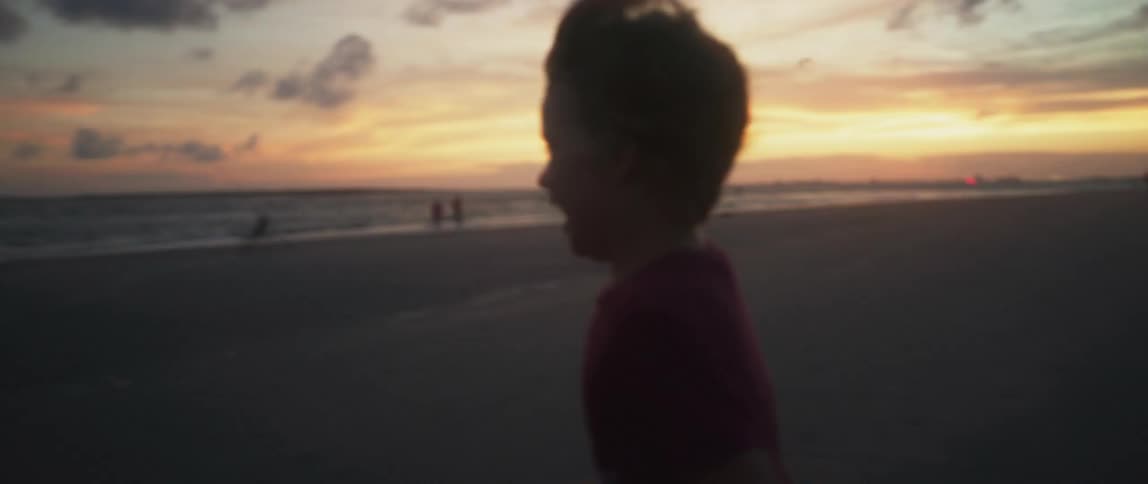 A young boy is running on a beach as the sun sets in the distance