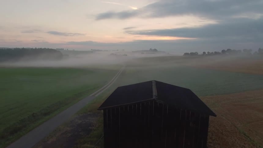 A barn in the middle of a large misty field