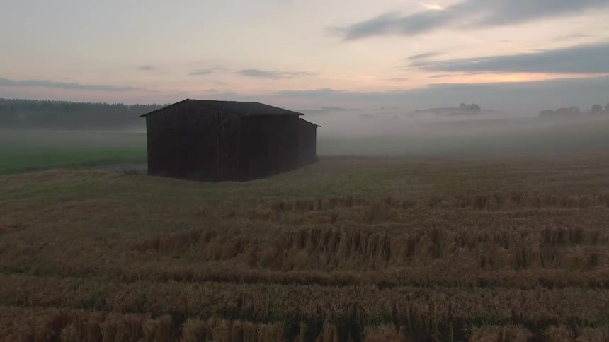 A barn in the middle of a large misty field
