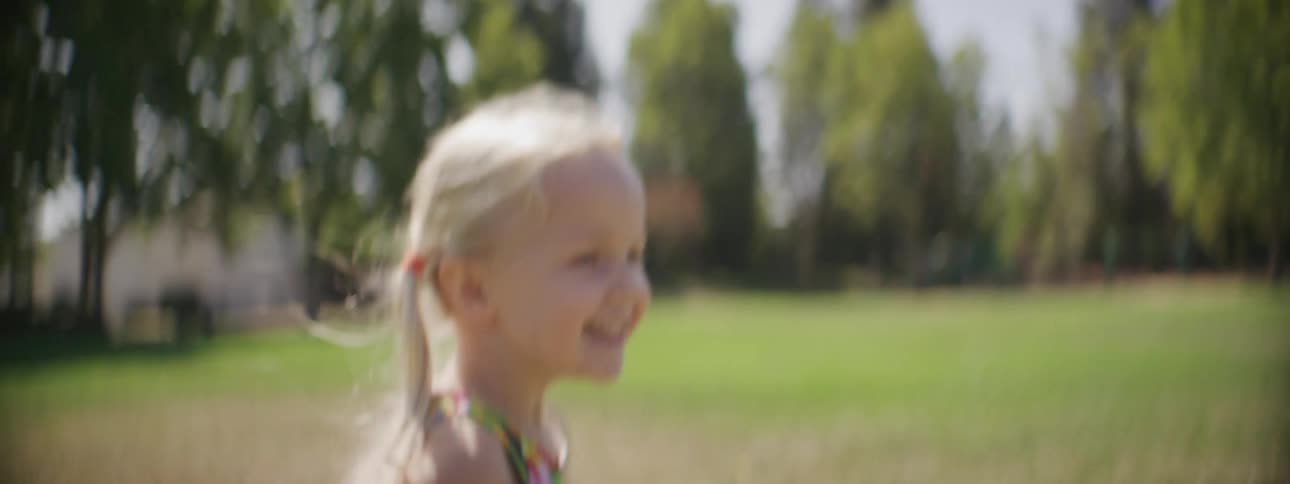 Blonde girl wearing colorful outfit smile while running across lawn