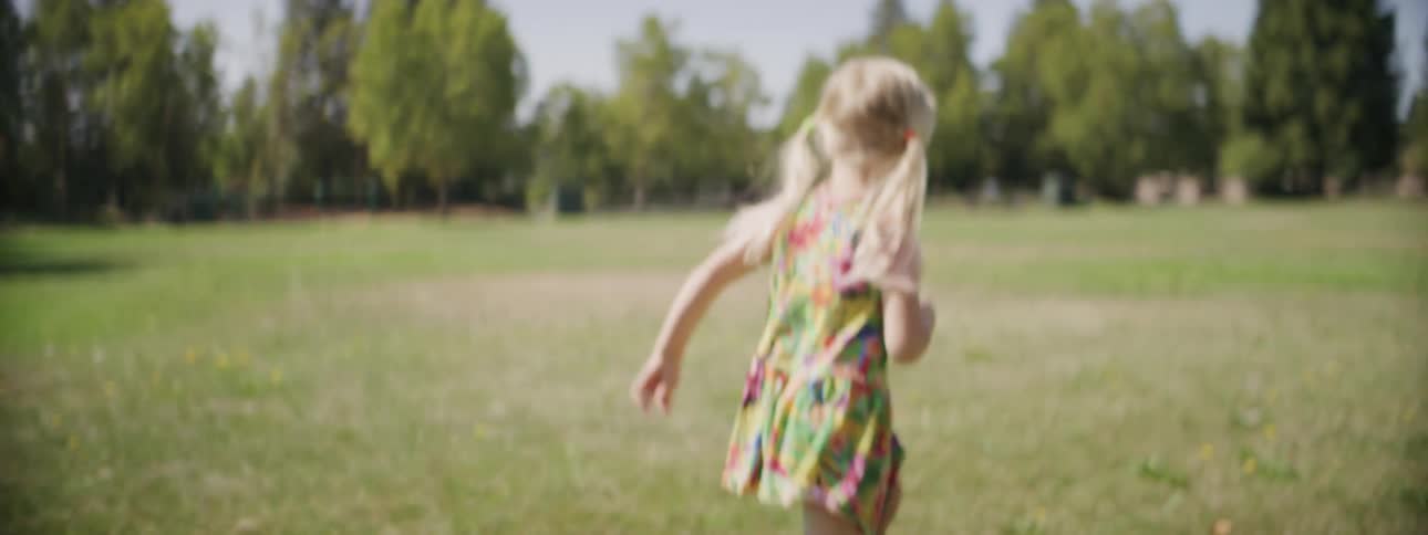 A girl runs through a field and picks up a dandelion