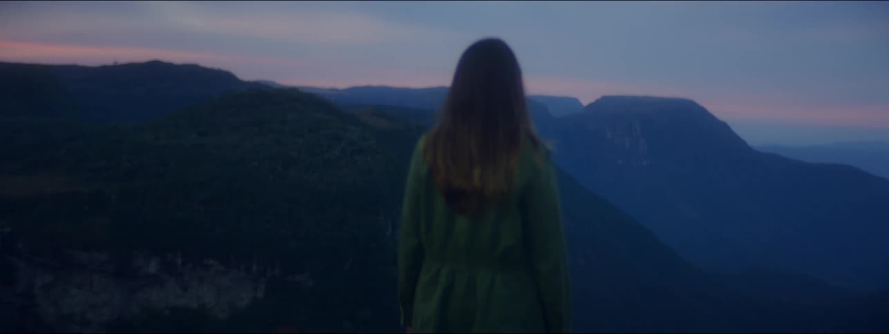 A young girl walks and stops and looks at the landscape of mountains after sunset
