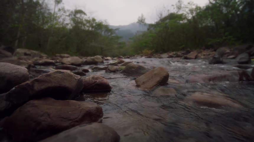 A river with water flowing over rocks and mountains in the background