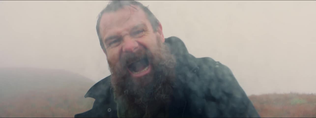 A man opens his mouth wide and screams while outside on a cloudy rainy day