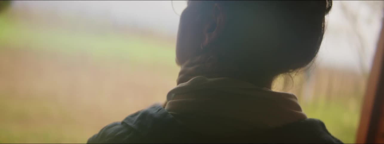 A woman is standing by a door looking outside and rubbing her neck
