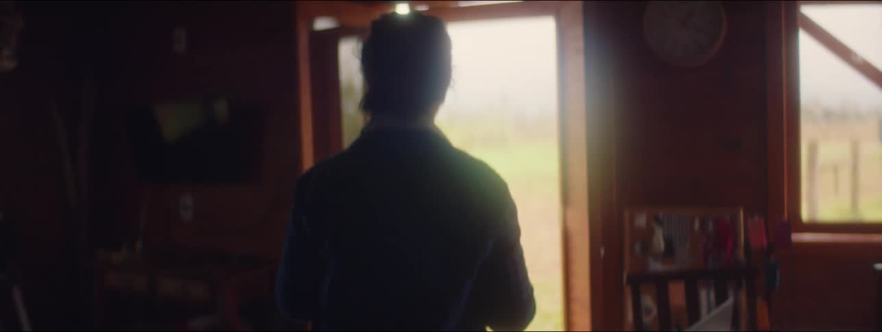 A woman pours herself a drink into a mug and goes to look out the cabin door