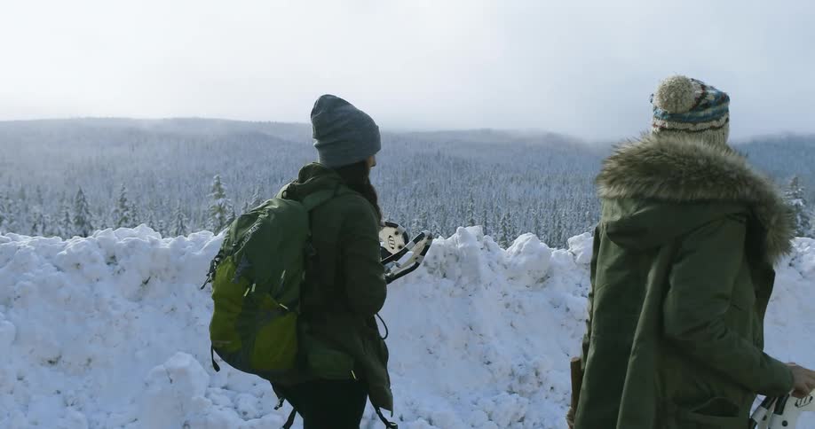 Two women carrying snowshoes walk away from their vehicle