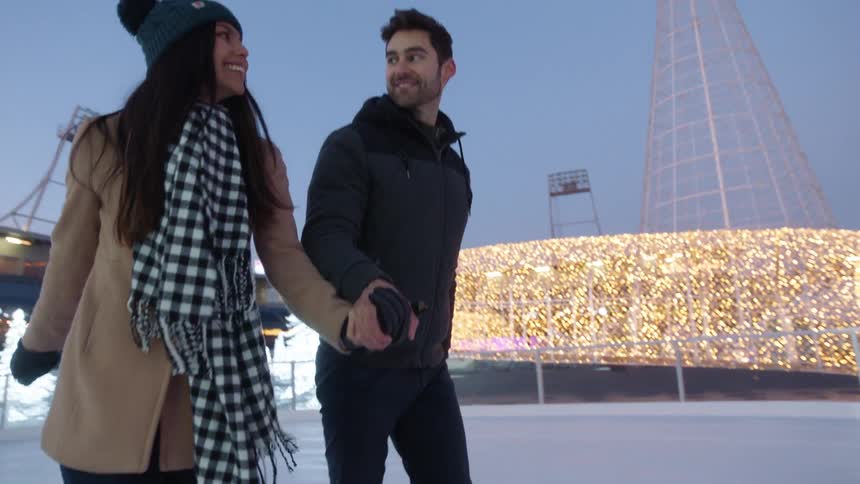 A couple hold hands while ice skating on a rink