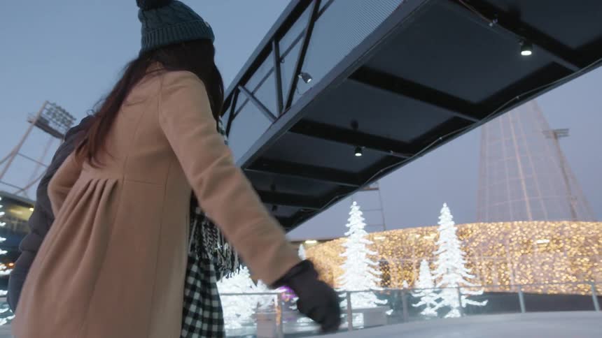 A man and woman ice skate while holding hands
