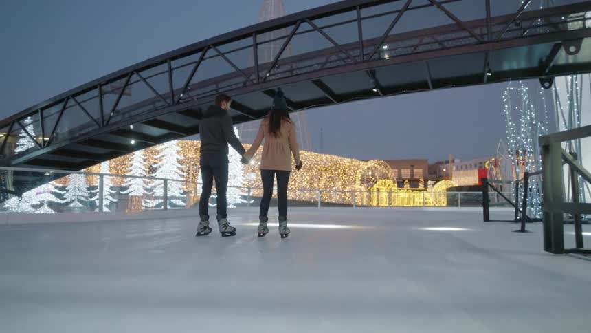 A couple are ice skating while holding hands