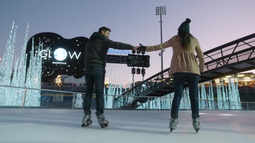 A man and woman skate on a rink while holding hands