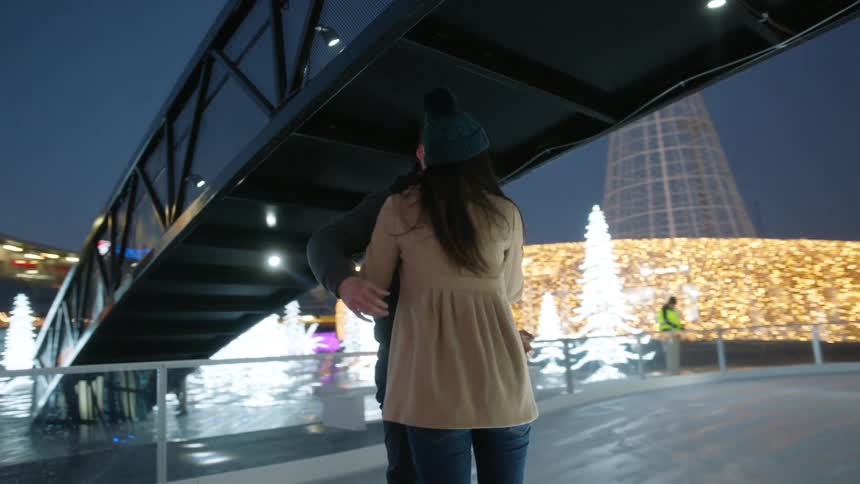 A couple holds on together while standing on ice with ice skates