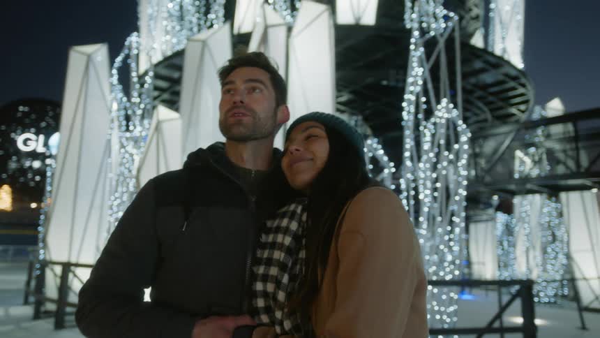 A man and a woman in front of decorations hugging and looking up at the sky