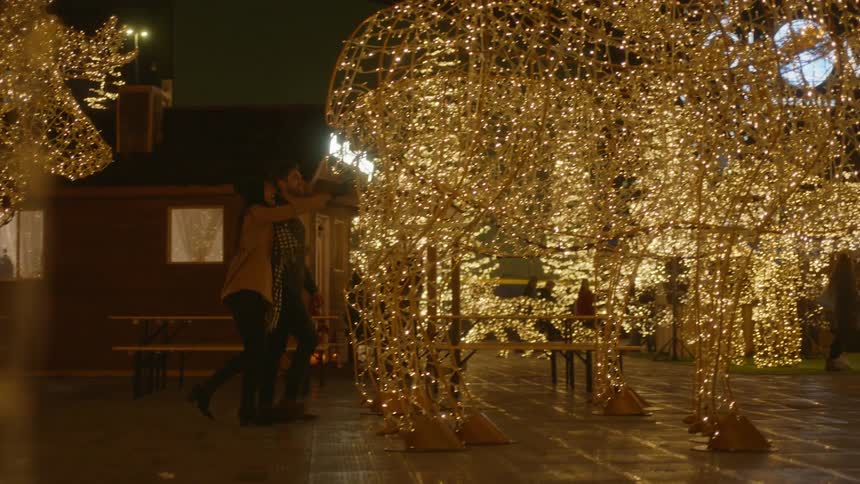 A man and woman holding hands while walking through a christmas holiday light display