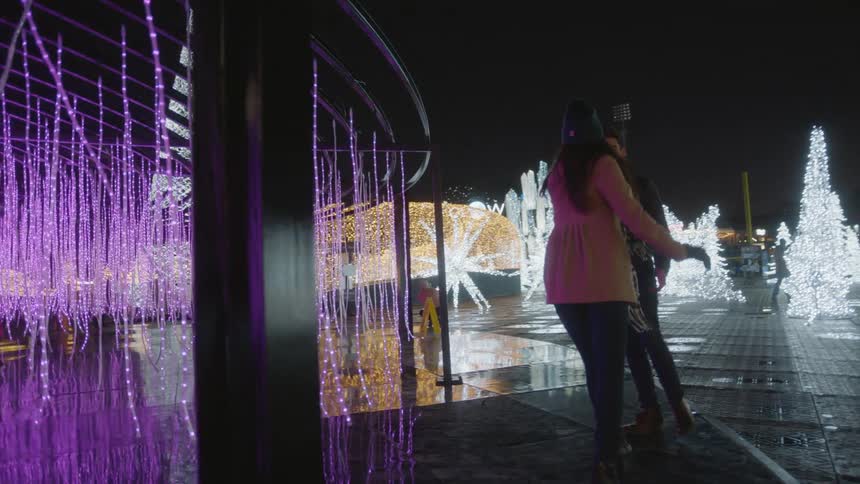 A couple walks through a christmas light display holding hands