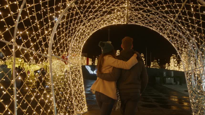 A couple walk through a christmas decorated tunnel