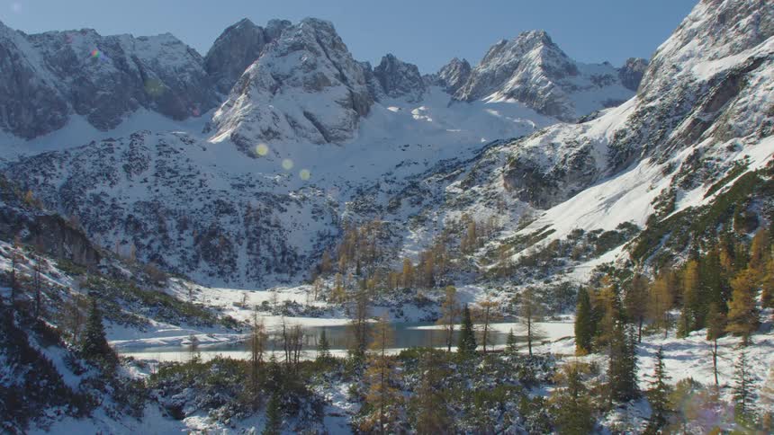 A small lake surrounded by trees and mountains partially covered in snow