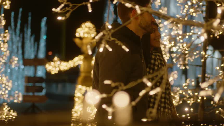 A man and woman hold hands as they walk through a holiday light display