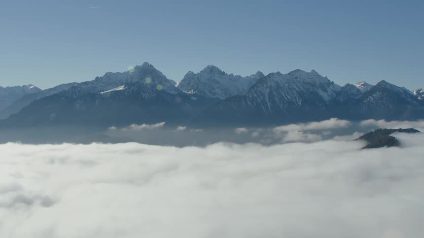 Aerial view of white clouds covering the terrain in front of the peaks of a mountain range