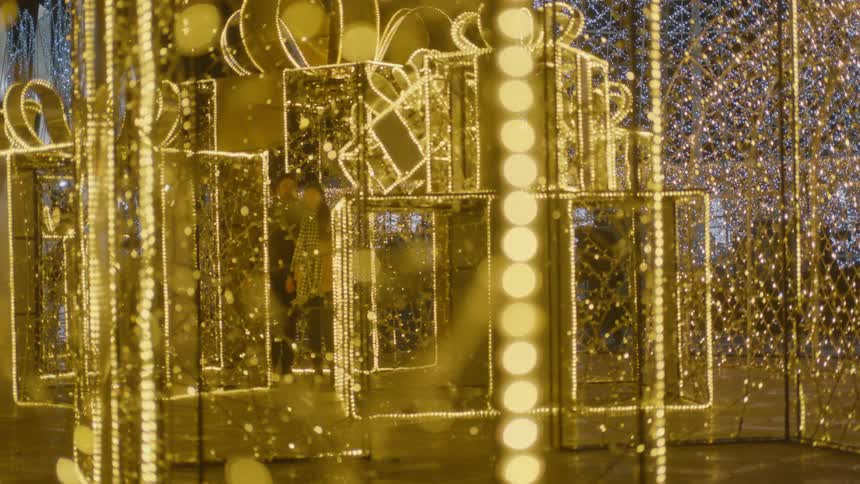 People walk through an outdoor christmas light display that looks like gift boxes